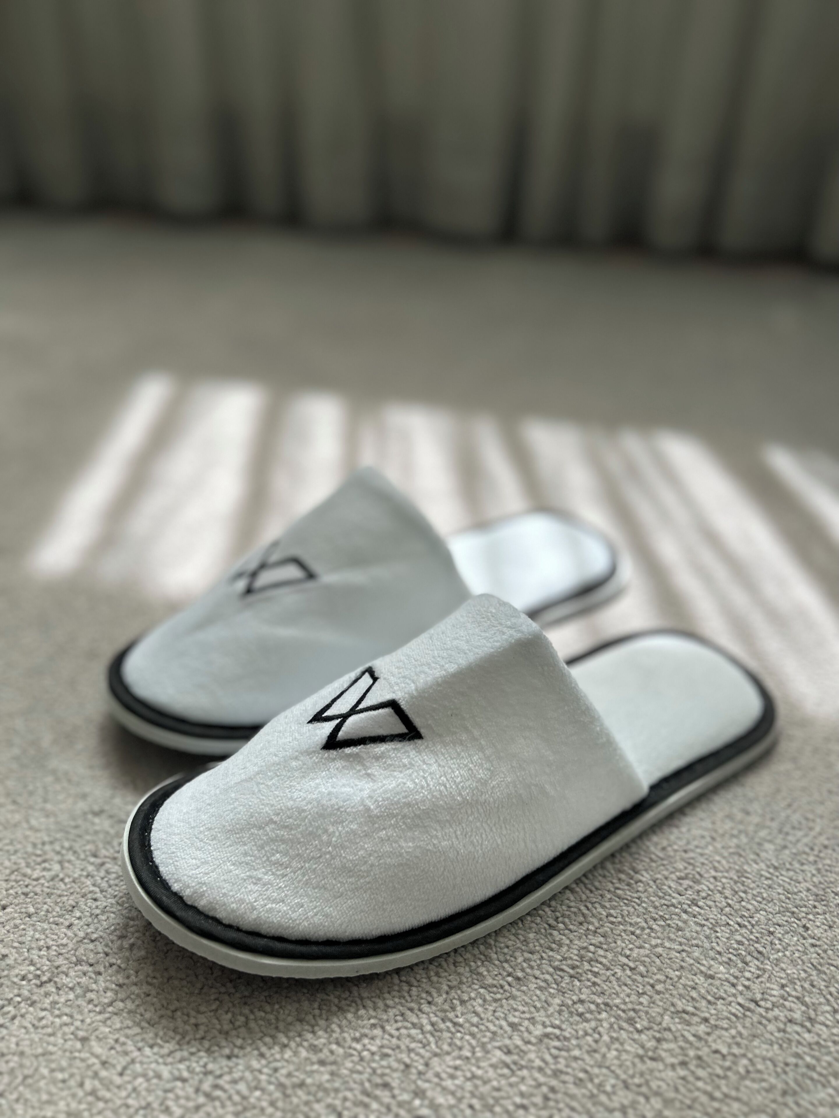 A pair of white slippers with a black logo on a textured carpet.