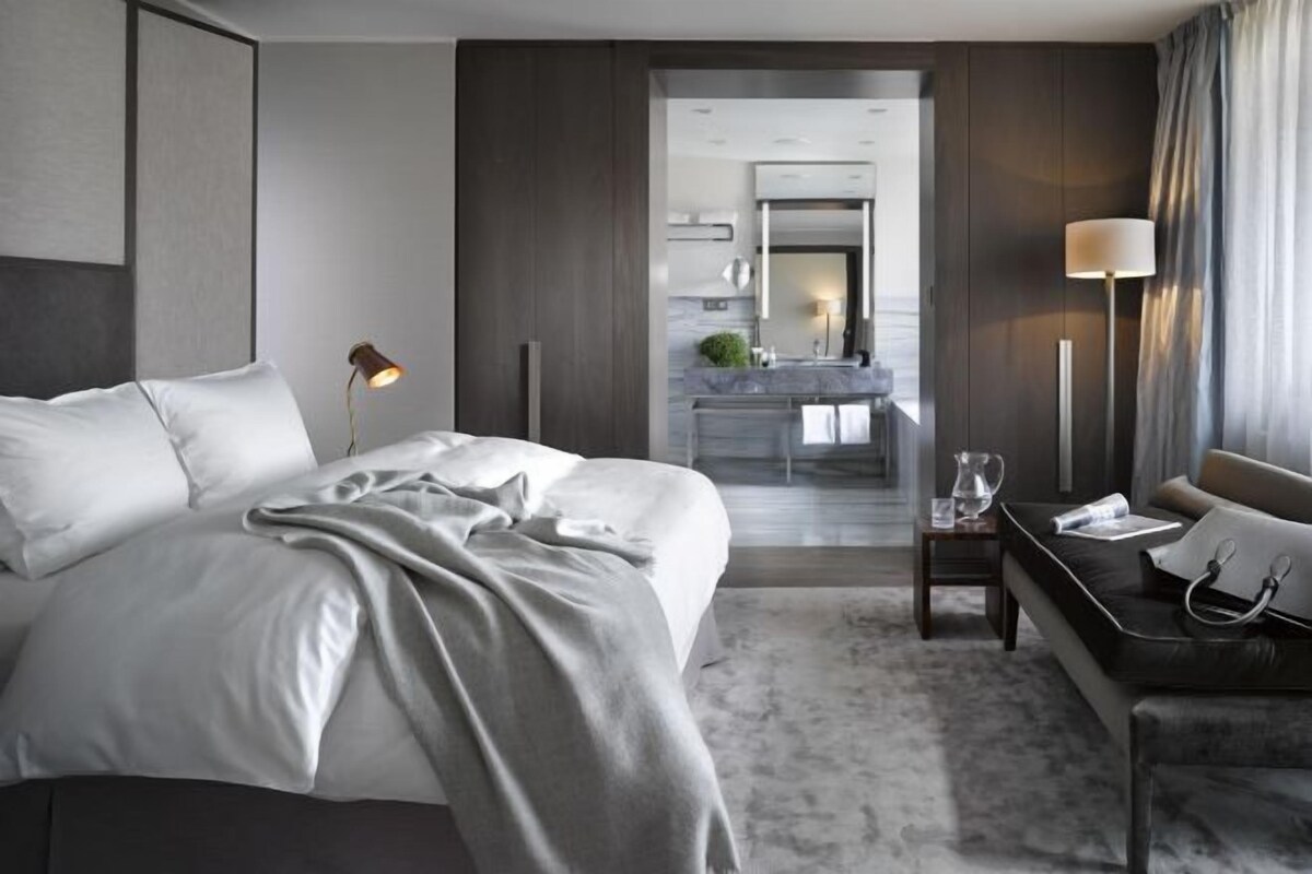Een hotelkamer met een bed, nachtkastje, lamp, en uitzicht op de badkamer en keuken.