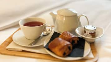 A neatly arranged breakfast tray on a bed with a cup of tea, a teapot, a small jar of honey, and a pastry.