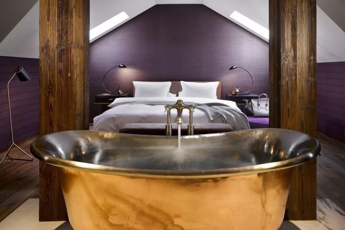 Een slaapkamer met een groot bad, een bed met witte lakens en een schuine balklaag.