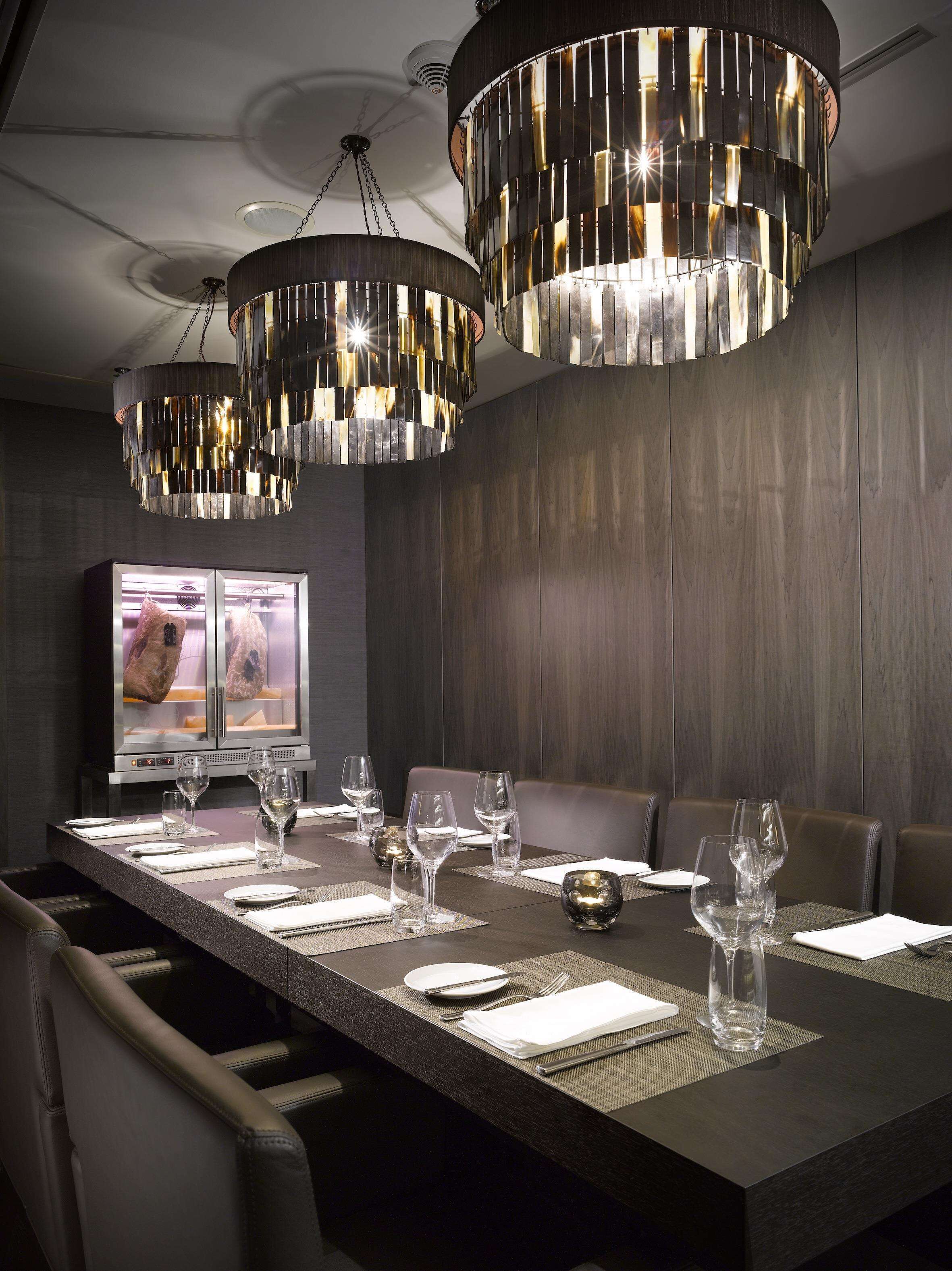 Un comedor moderno con una mesa larga dispuesta para una comida, elegantes candelabros y un televisor mostrando un menú.