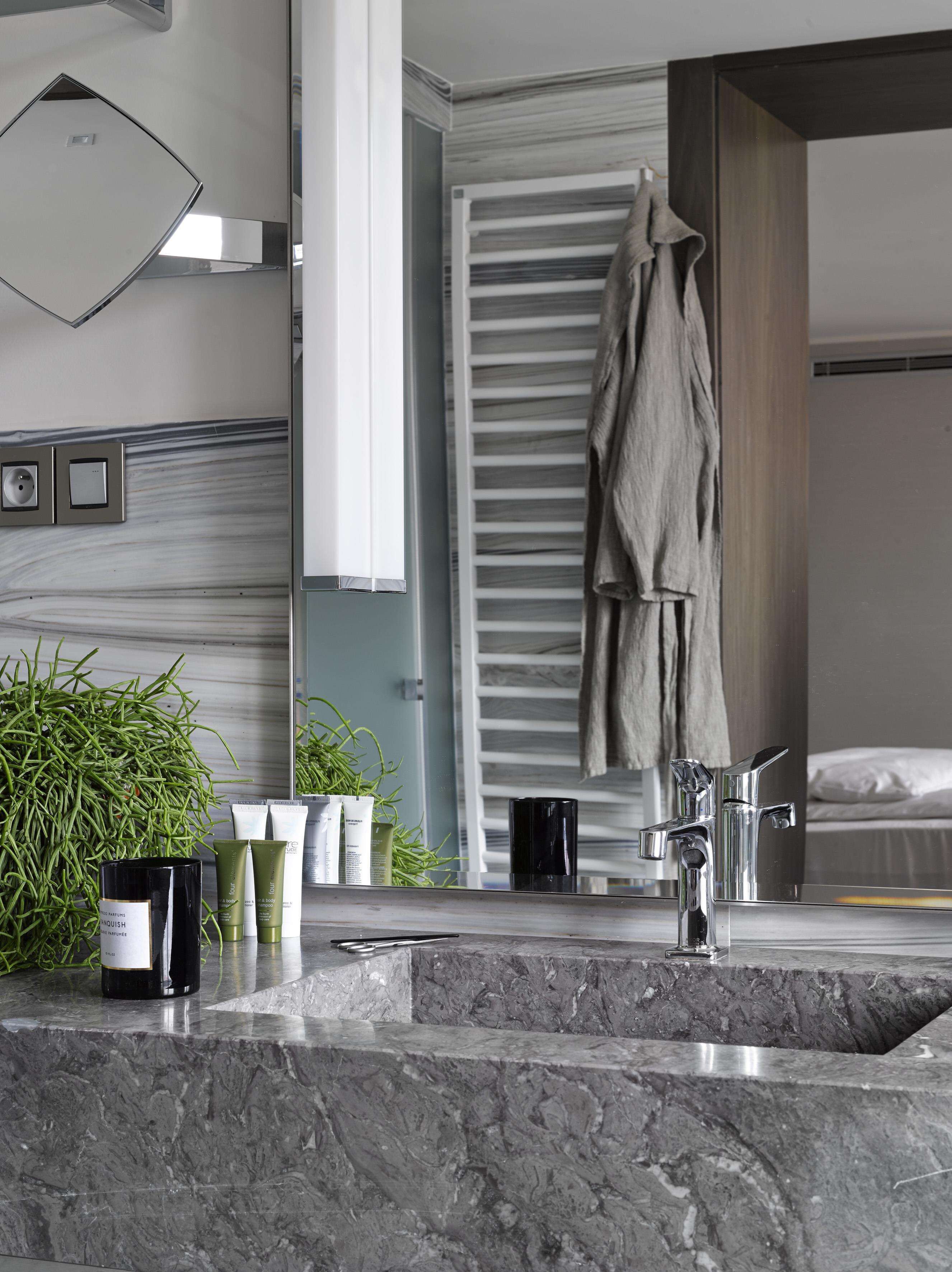 A modern bathroom with a marble sink, a large mirror, and a towel rack.