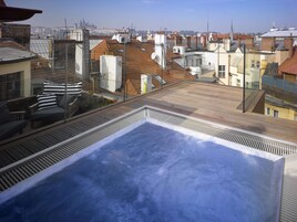 Terraço no telhado com hidromassagem, guarda-corpo de vidro e vista para o horizonte urbano.