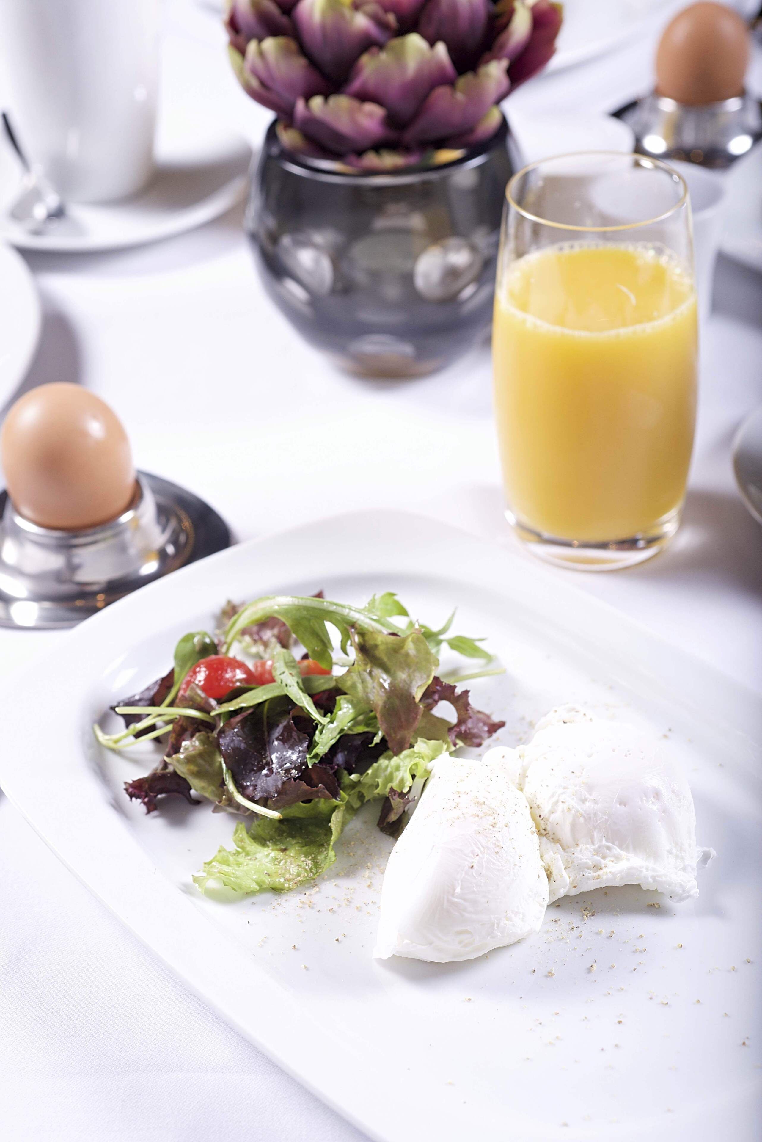 A white plate with a salad, a glass of orange juice, and a white food item, possibly cheese, on a white tablecloth.