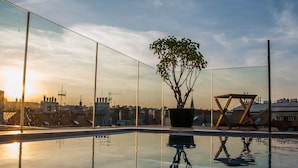A rooftop pool with a potted tree and a wooden structure, reflecting the cityscape and sunset. - The Emblem Prague Hotel  (Prague)