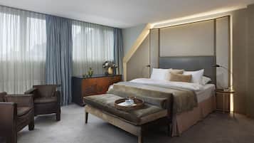 Habitació d'hotel moderna amb un llit gran, una zona de seients amb una banca, un escriptori i una finestra gran amb cortines.