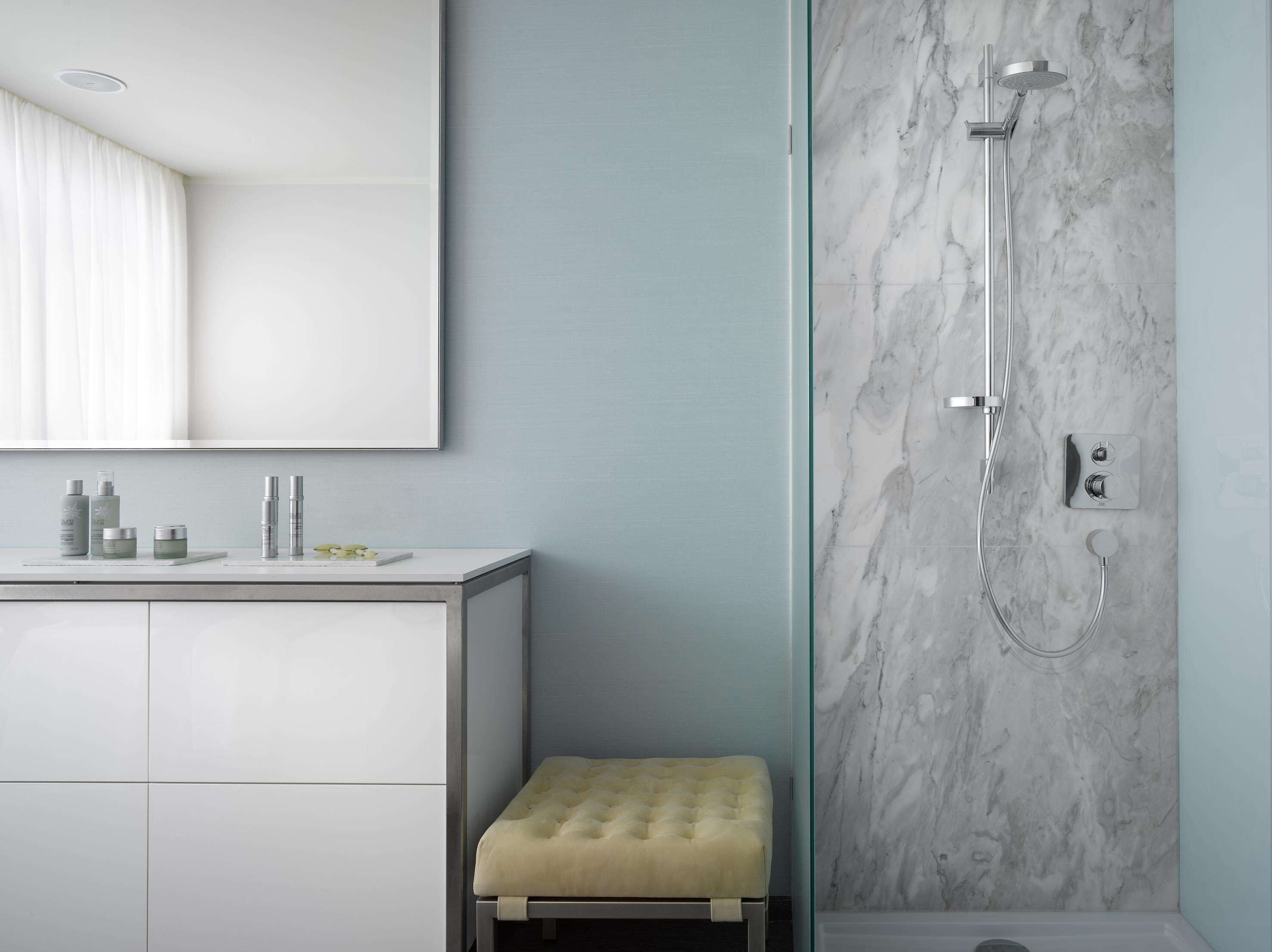 Een moderne badkamer met een marmeren douche, een wastafel met toiletartikelen en een comfortabele kruk.