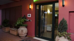 A hotel entrance with a neon sign, potted plants, and a glass door. - Albergo Bar Cenni (Ravenna)