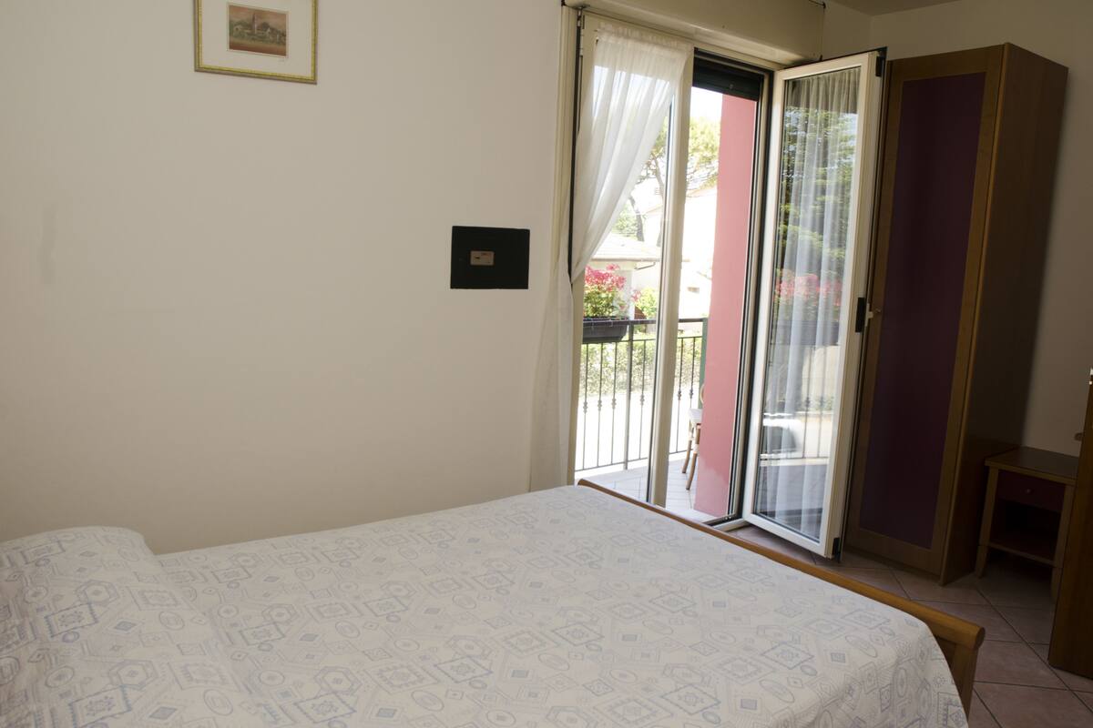 Quarto com cama, porta de vidro deslizante para uma varanda e um guarda-roupa.