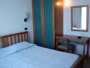 A bedroom with a bed, a desk, a chair, a mirror, and a wall-mounted light. - Albergo Bar Cenni (Ravenna)
