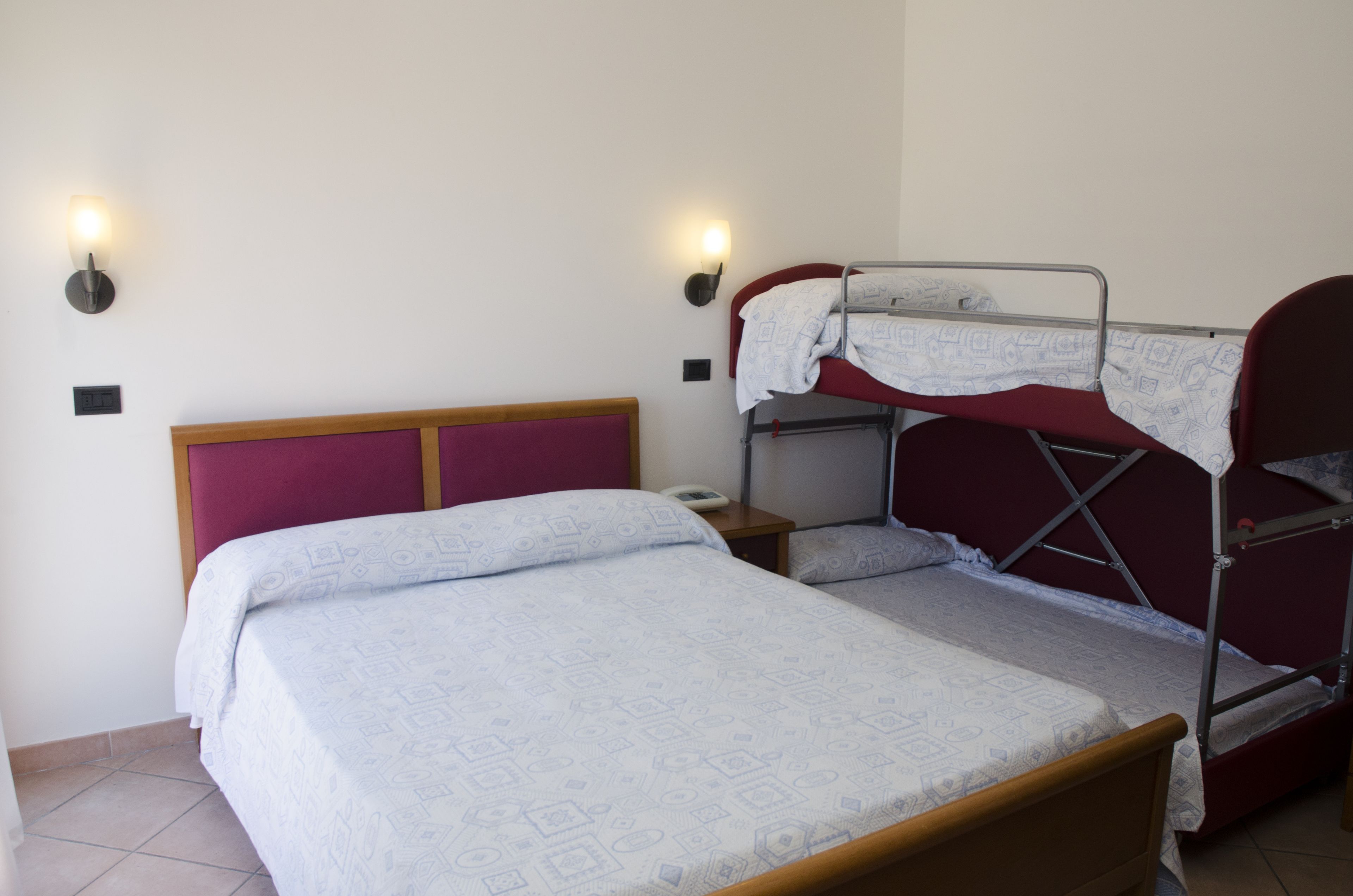 A room with a single bed, a bunk bed, a bedside table, and two wall-mounted lights.