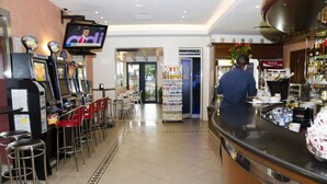 A bar area with a television screen, bar stools, and a counter with various items. - Albergo Bar Cenni (Ravenna)