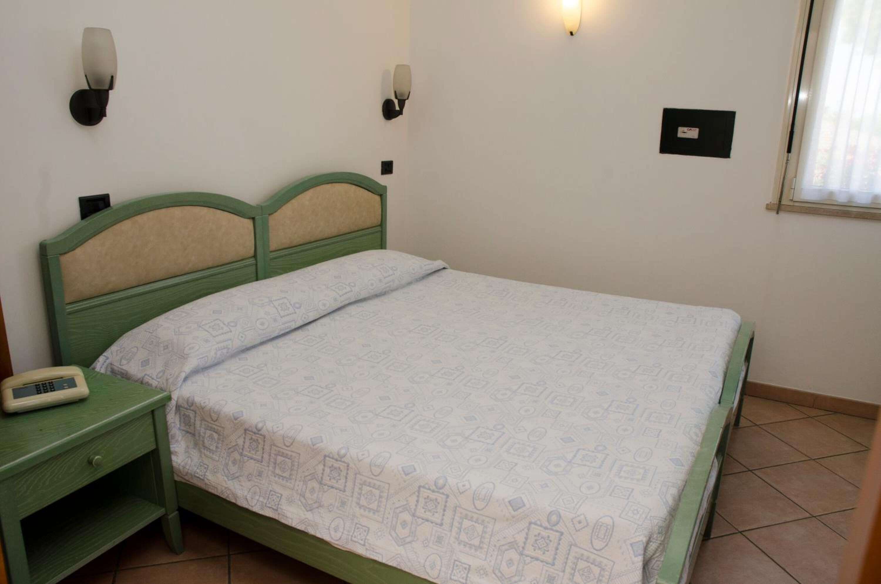Ein Einzelbett mit einem gemusterten Bettbezug, ein Nachttisch mit Telefon und zwei Wandleuchten.