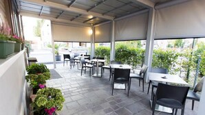 An outdoor patio area with tables and chairs, potted plants, and a covered roof. - Albergo Bar Cenni (Ravenna)