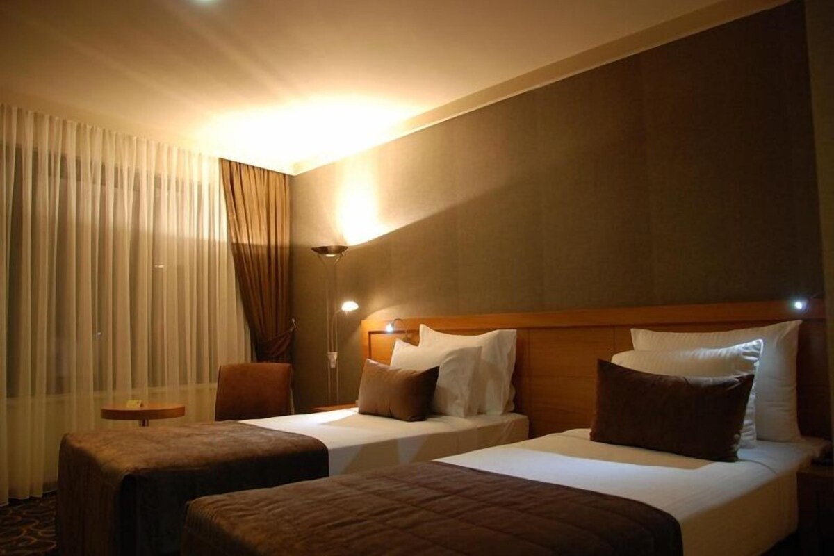 Habitación de hotel con dos camas, una mesita de noche, una lámpara y una silla.