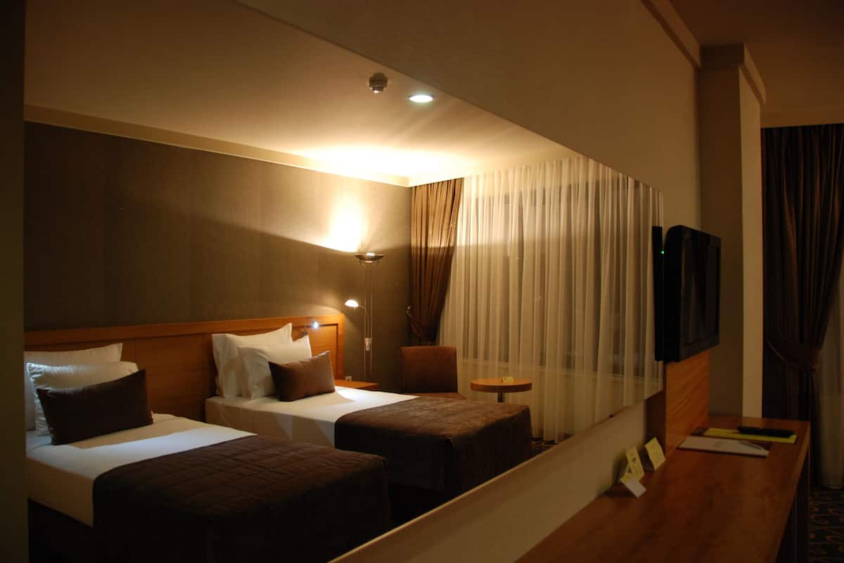 A hotel room with two beds, a small table, a TV, and a mirror.