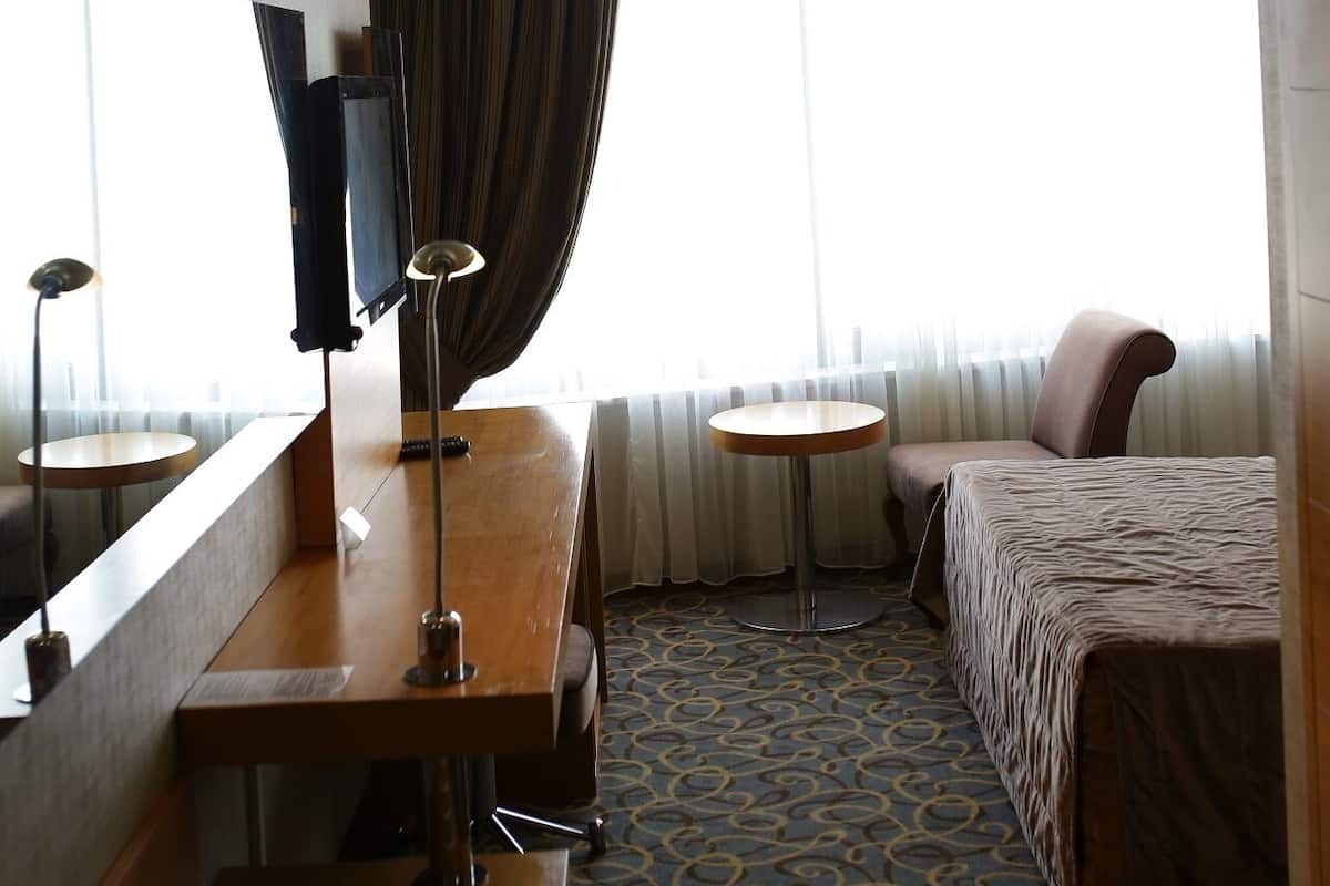 A hotel room with a bed, a desk, a chair, a TV, and a window with curtains.