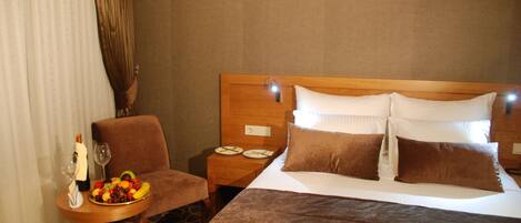 Habitación de hotel con una cama grande, una mesita de noche de madera con un cuenco de frutas, una botella de champán y una copa de vino.