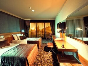 A hotel room with two beds, a desk, a chair, a TV, and a large window with curtains. - Volley Hotel İzmir (Izmir)