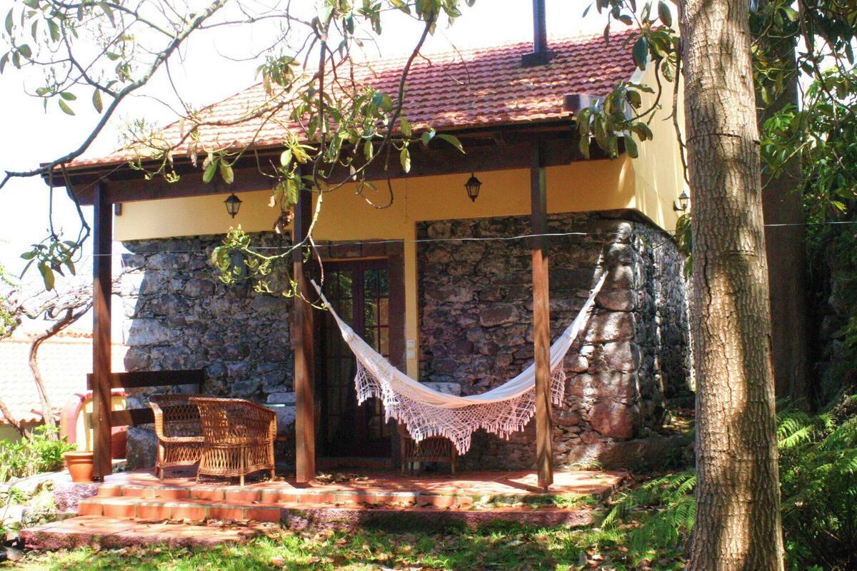 A stone building with a red-tiled roof, a hammock, and wicker furniture on a brick patio.