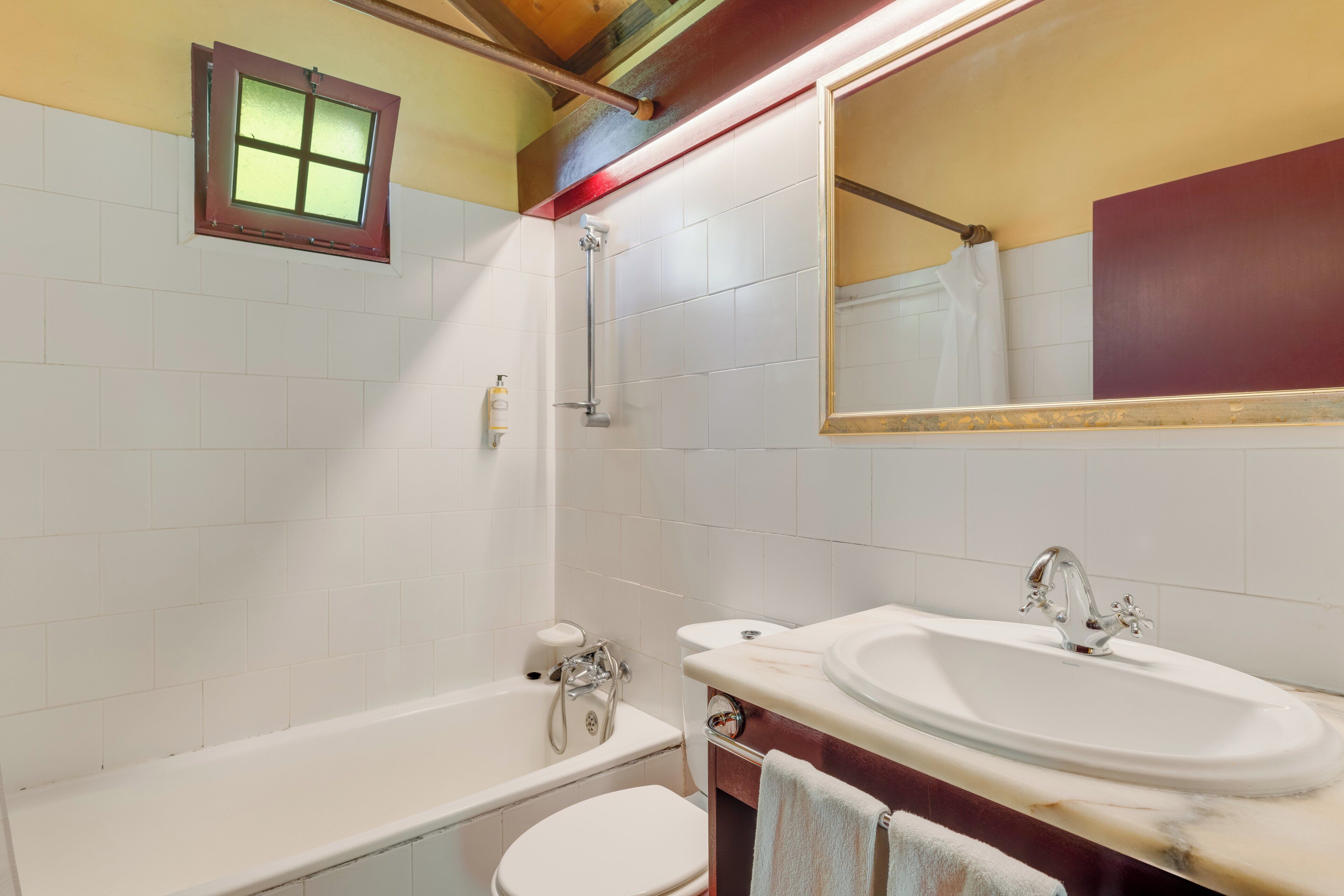 Een badkamer met een bad, toilet, wastafel en een klein raam.