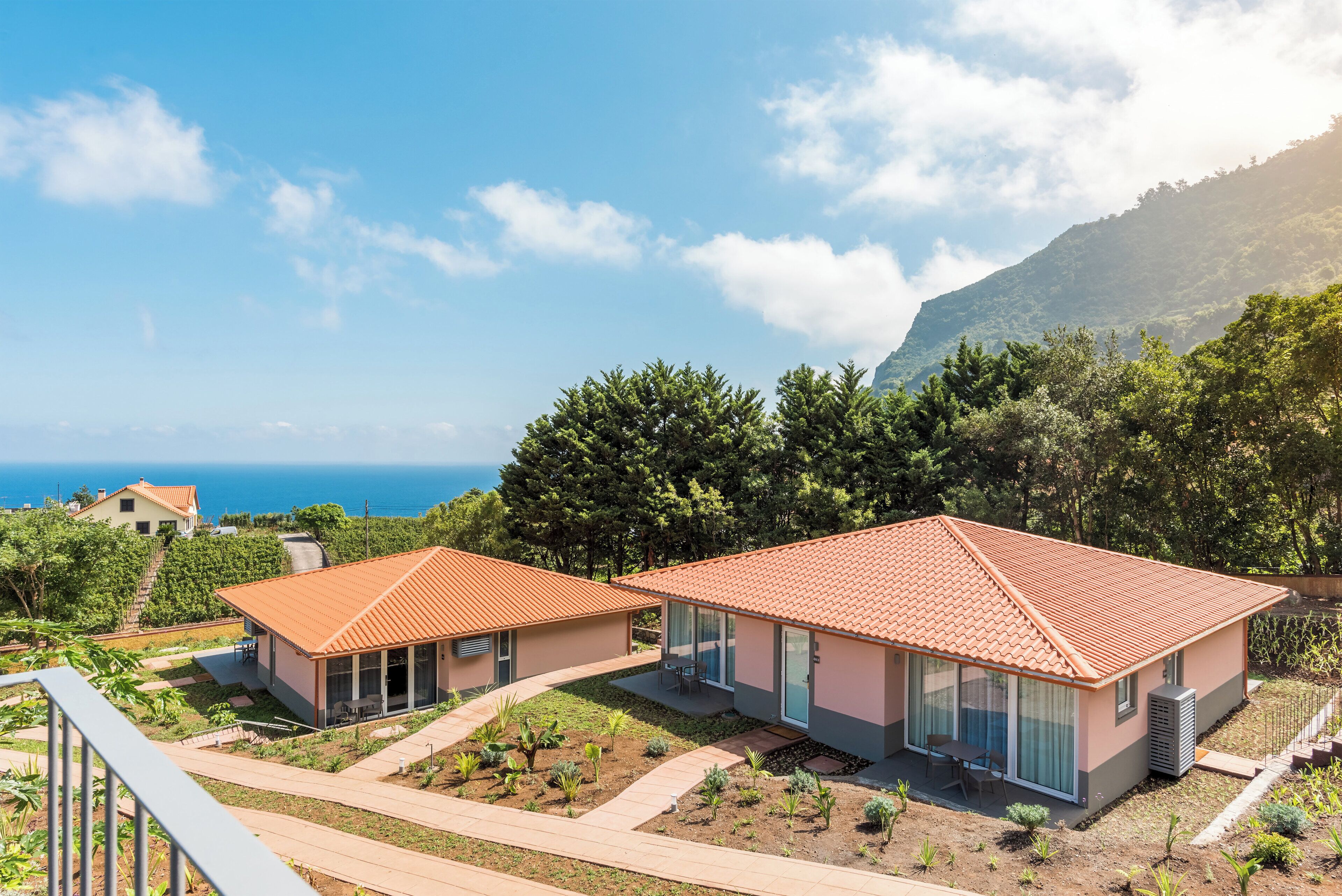 Two modern houses with red-tiled roofs, a patio, and a view of the sea.