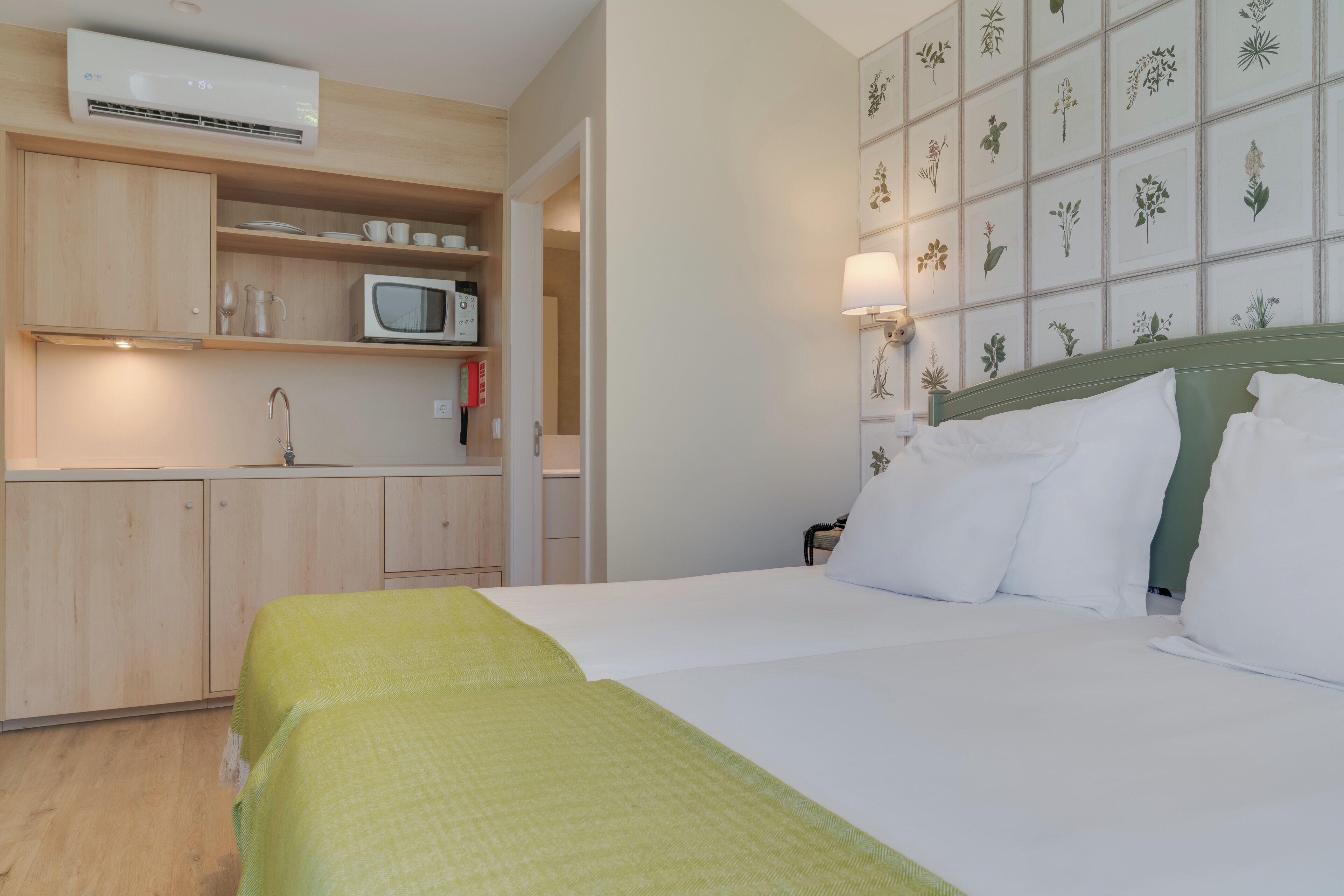 Hotelkamer met een bed, een magnetron, een spoelbak en een wand met botanische prints.