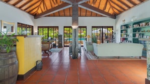 A spacious interior with a high wooden ceiling, tiled floor, and a central column. There are bookshelves, a sofa, and a dining area visible. - Pestana Quinta do Arco Nature & Rose Garden Hotel (Santana)