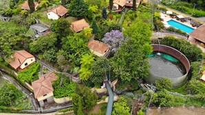 An aerial view of a residential area with houses, a swimming pool, and a circular water feature. - Pestana Quinta do Arco Nature & Rose Garden Hotel (Santana)