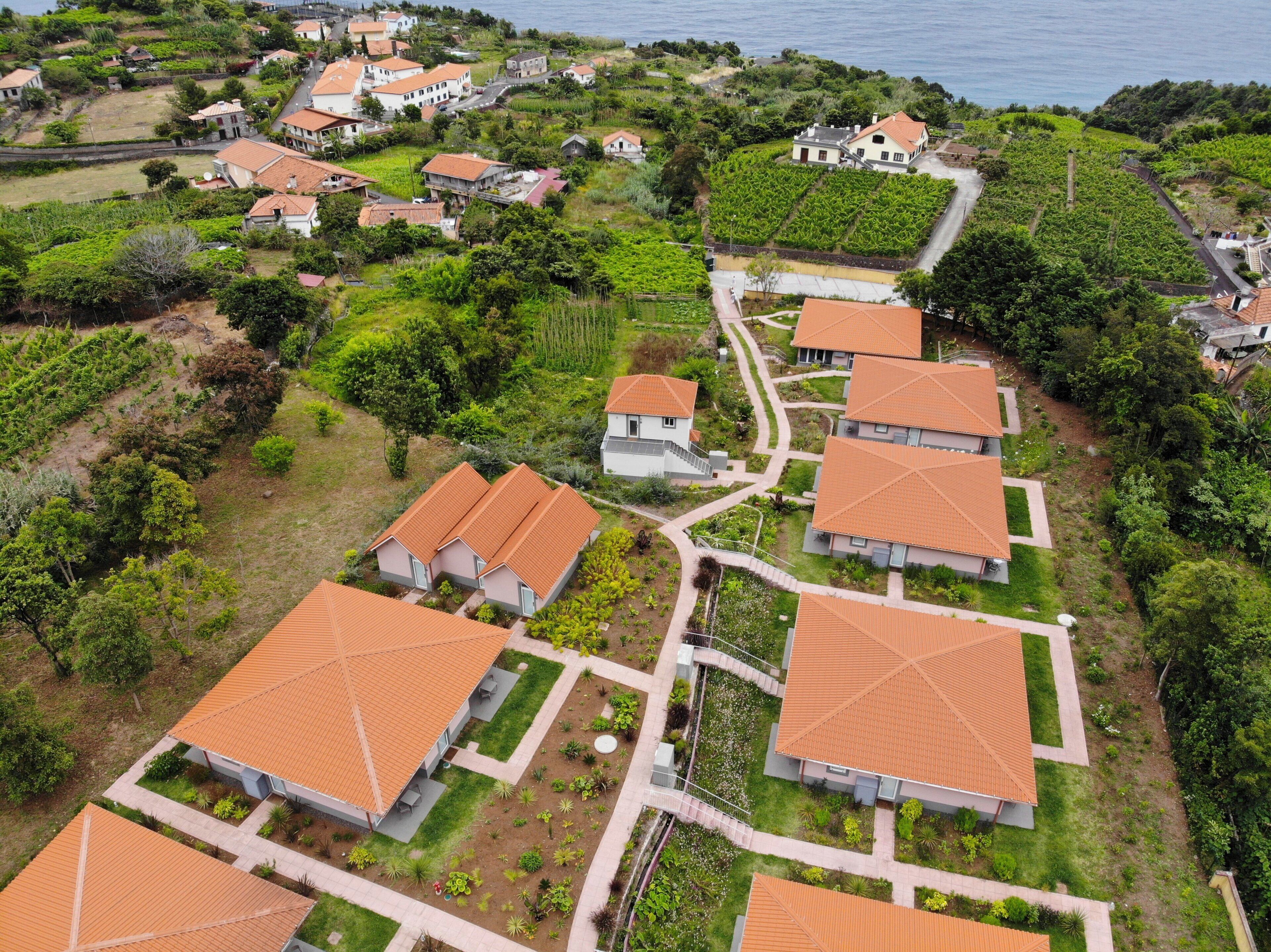 Vista aérea de una zona residencial con casas de techo de tejas rojas, rodeada de vegetación y una costa.