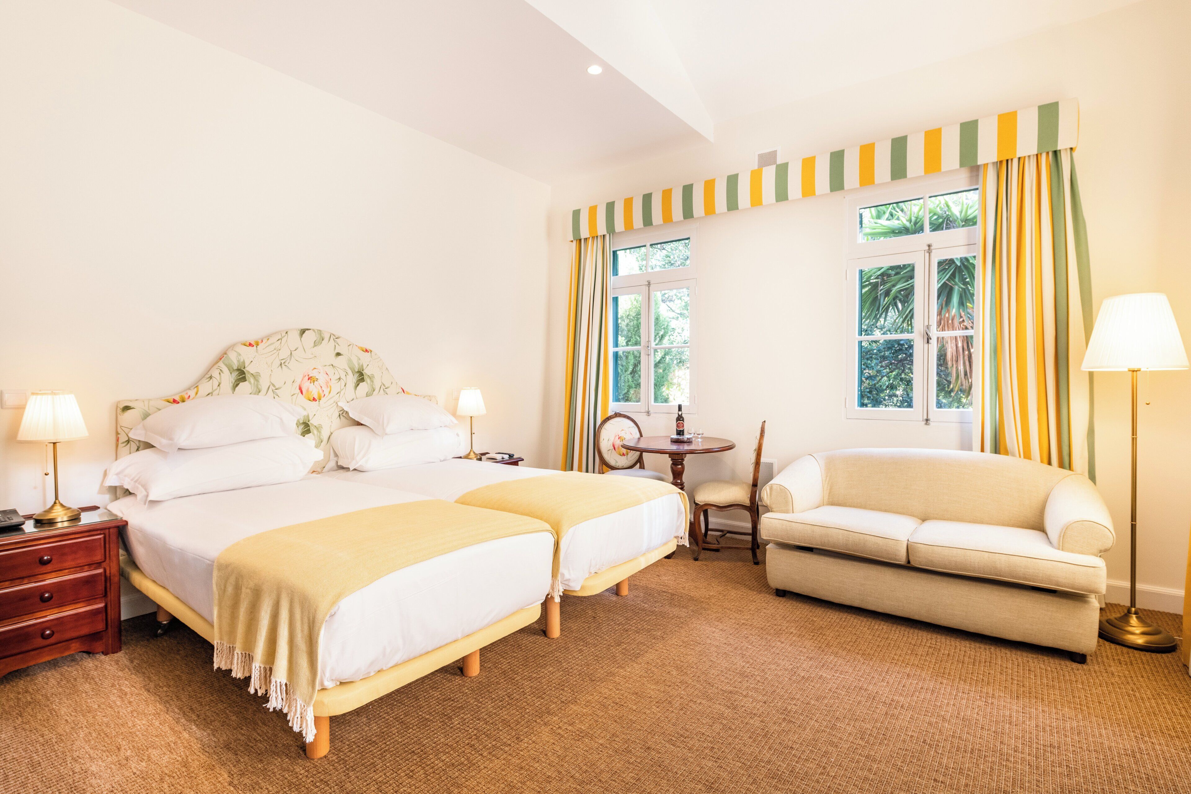 A hotel room with a double bed, a sofa, a small table, and a chair.