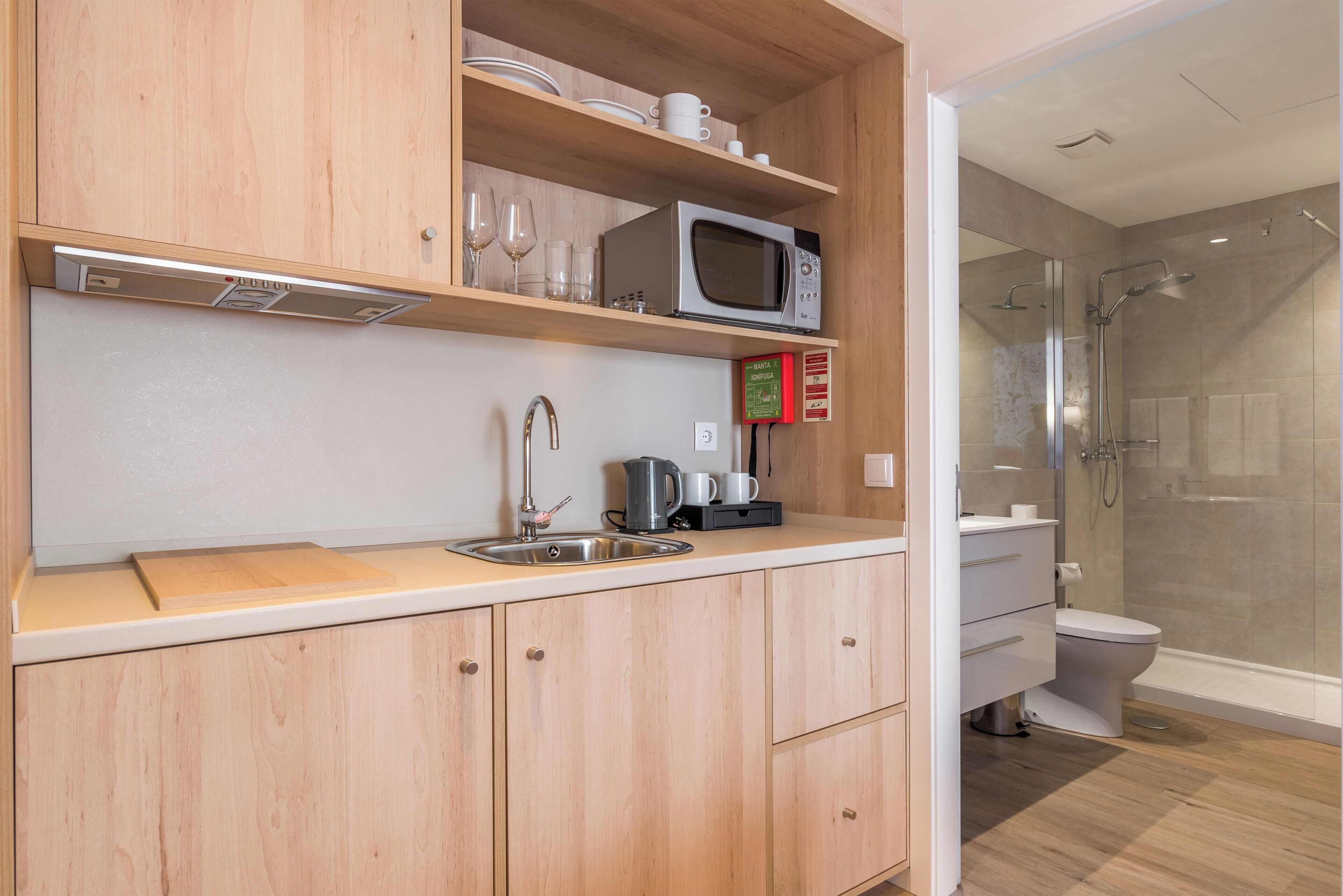 A modern kitchen with a microwave, sink, and cabinets, and a separate bathroom with a shower and toilet.