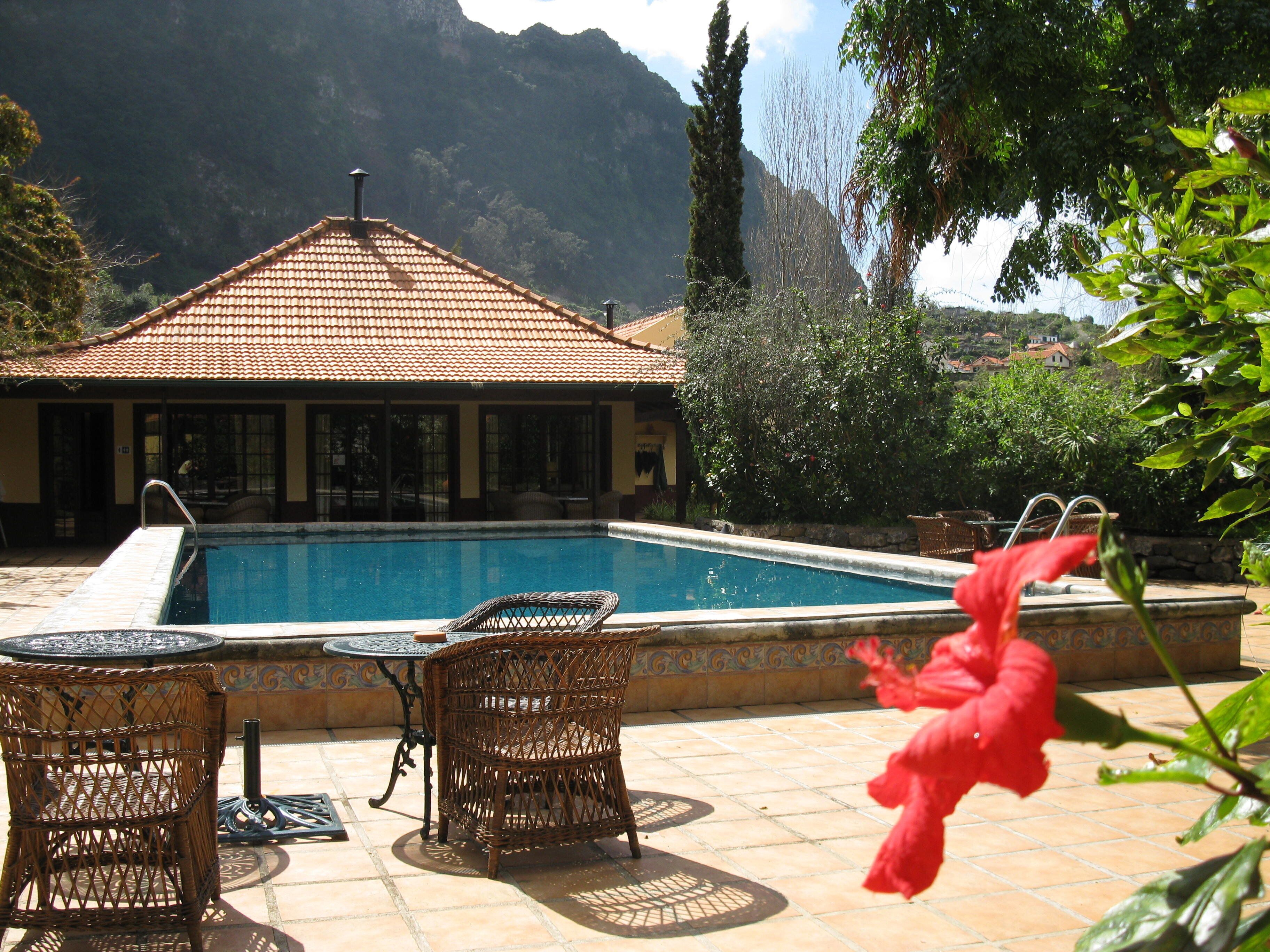 Zona de piscina con techo de baldosas, mobiliario de mimbre y vistas a montañas.