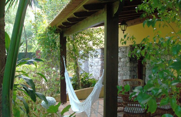 A covered outdoor area with a hammock, wicker furniture, and a stone wall. - Pestana Quinta do Arco Nature & Rose Garden Hotel (Santana)