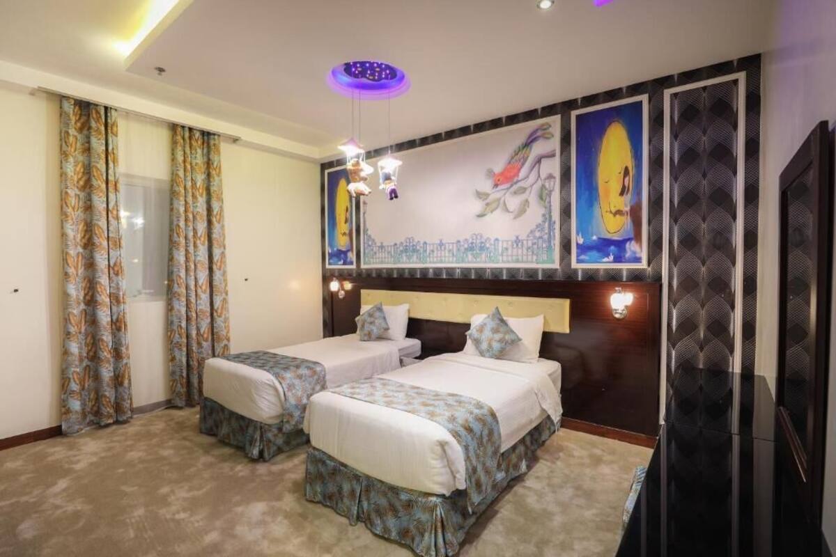 Habitación de hotel con dos camas, un mural grande, un televisor de pantalla plana y una lámpara en el techo.