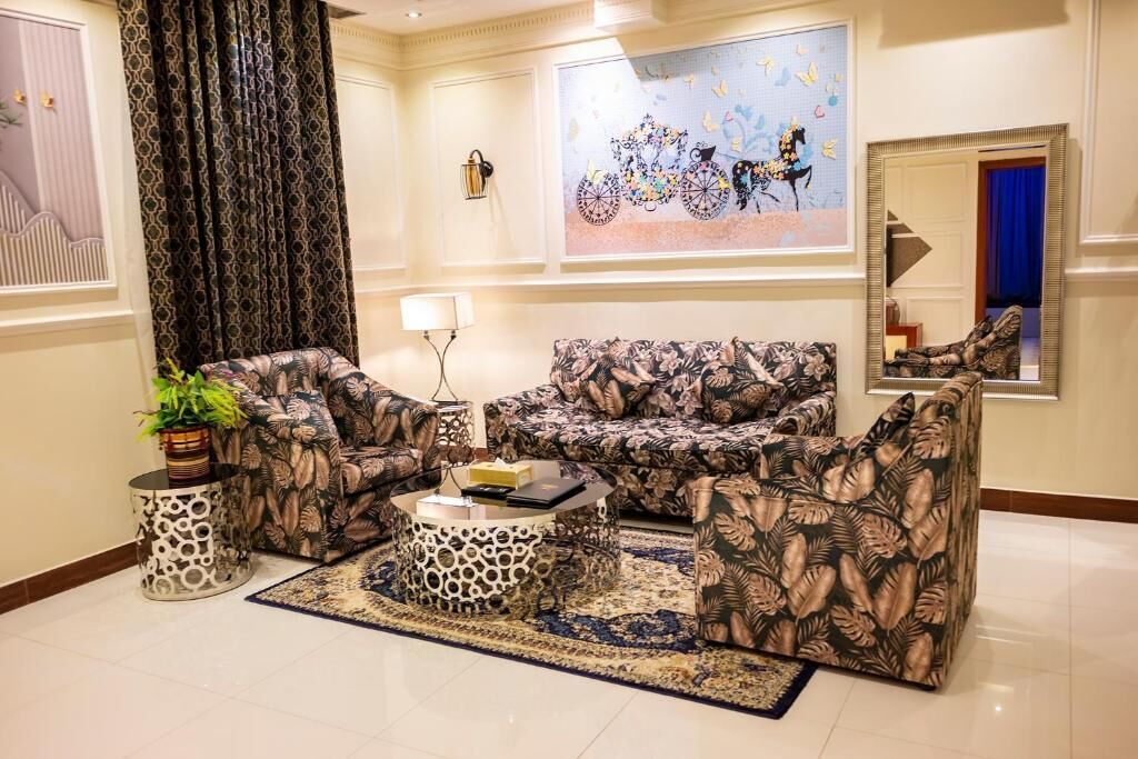 A living room with patterned sofas, a coffee table, a rug, a potted plant, and a wall painting.