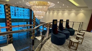 A modern hotel lobby with a glass railing, a large chandelier, and blue seating areas. - Meral Crown Hotel (Riyadh)