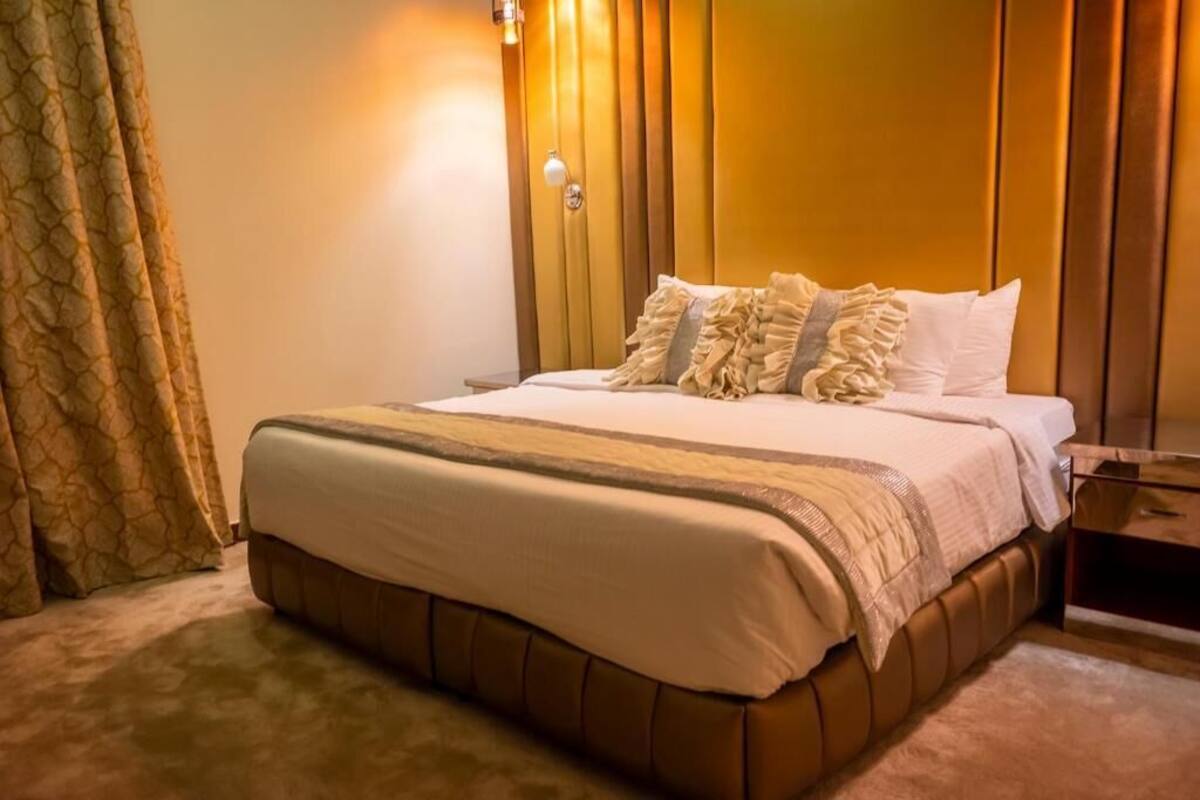 Una habitación de hotel con una cama grande, una mesita de noche, una lámpara y una cortina.