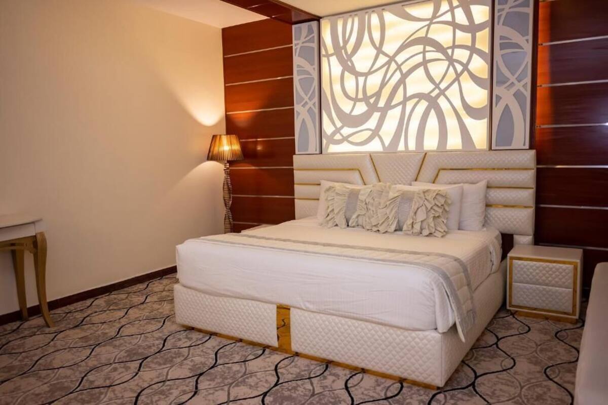 Habitación de hotel con una cama grande, una mesita de noche, una lámpara y un panel decorativo en la pared.