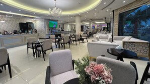 A modern hotel lobby with a bar area, seating arrangements, and a large window offering a view of the outside. - Meral Crown Hotel (Riyadh)