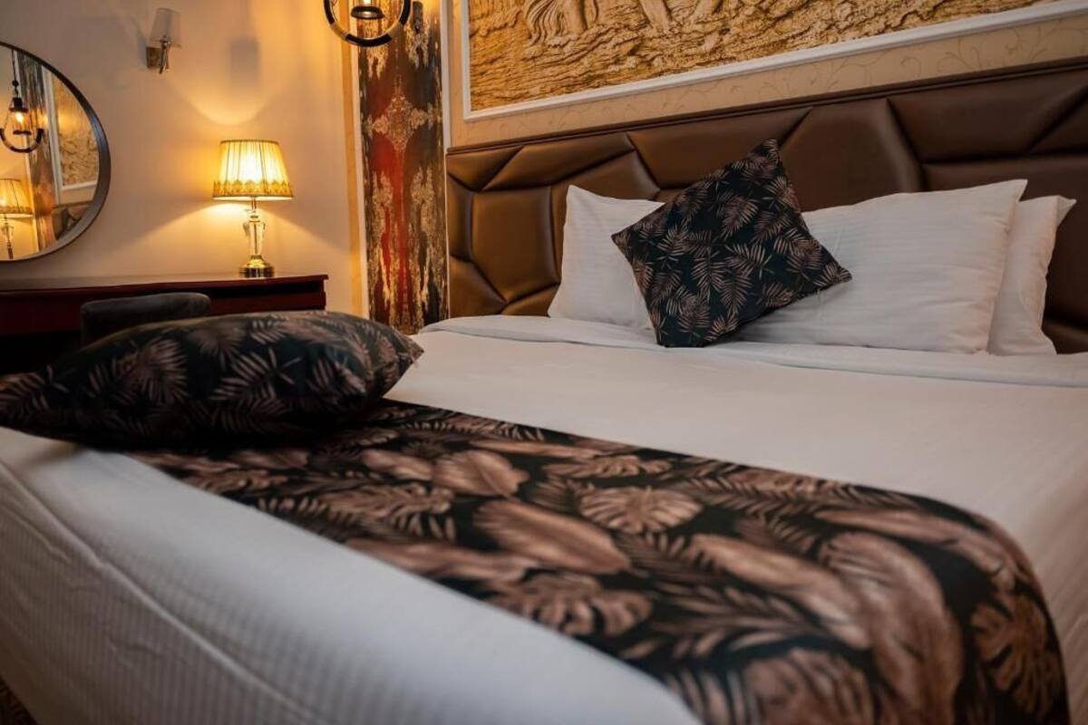 Una habitación de hotel con cama, mesita de noche, lámpara, espejo y pared con textura.