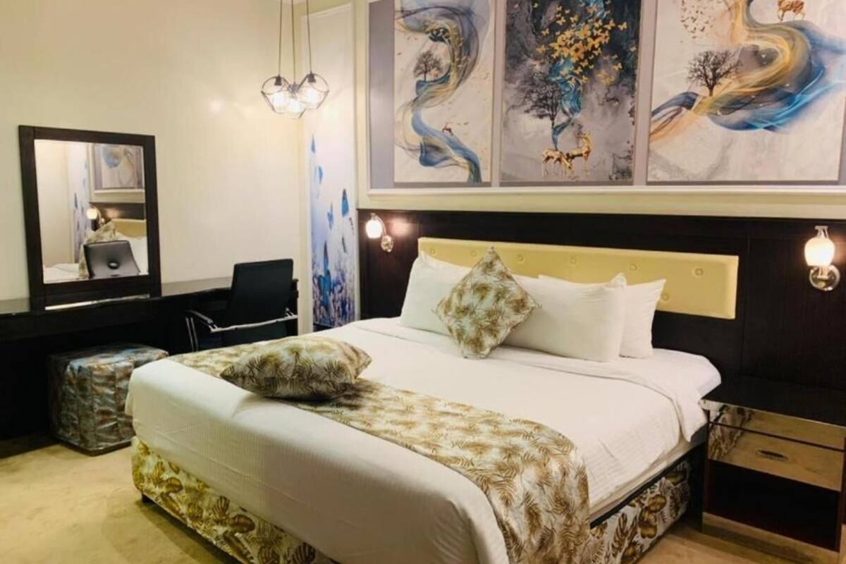 Habitación de hotel con cama, escritorio, silla, espejo y obras de arte en la pared.