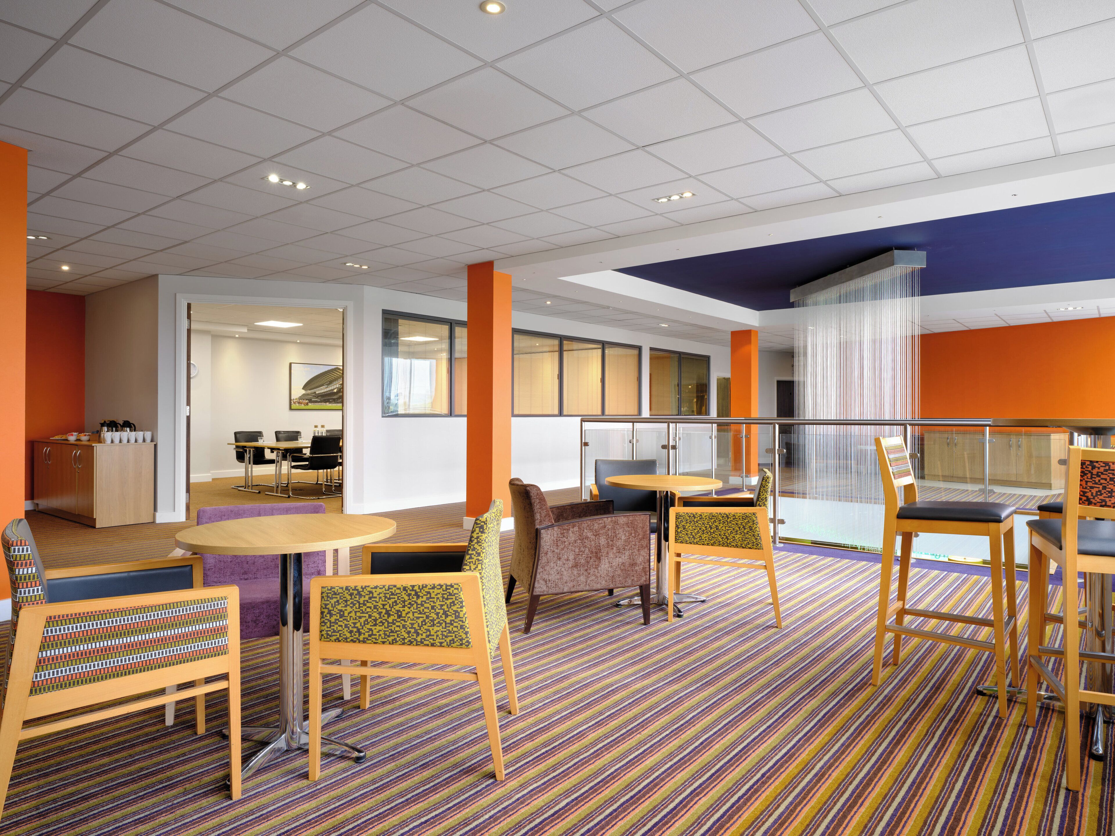 A modern hotel lobby with a striped carpet, wooden furniture, and a glass railing overlooking a balcony.