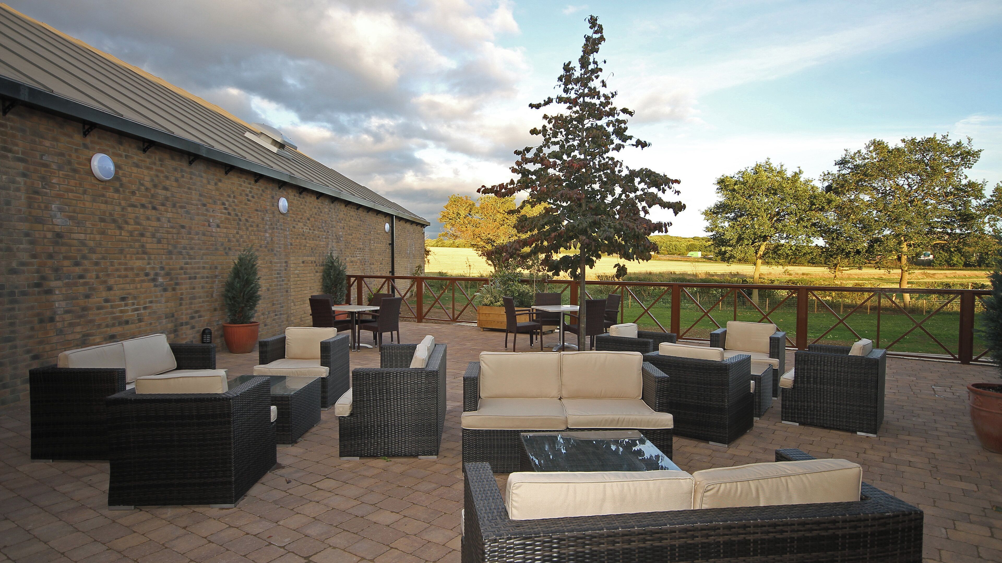 Un patio al aire libre con mobiliario de mimbre, una pared de ladrillo y vistas a un campo.