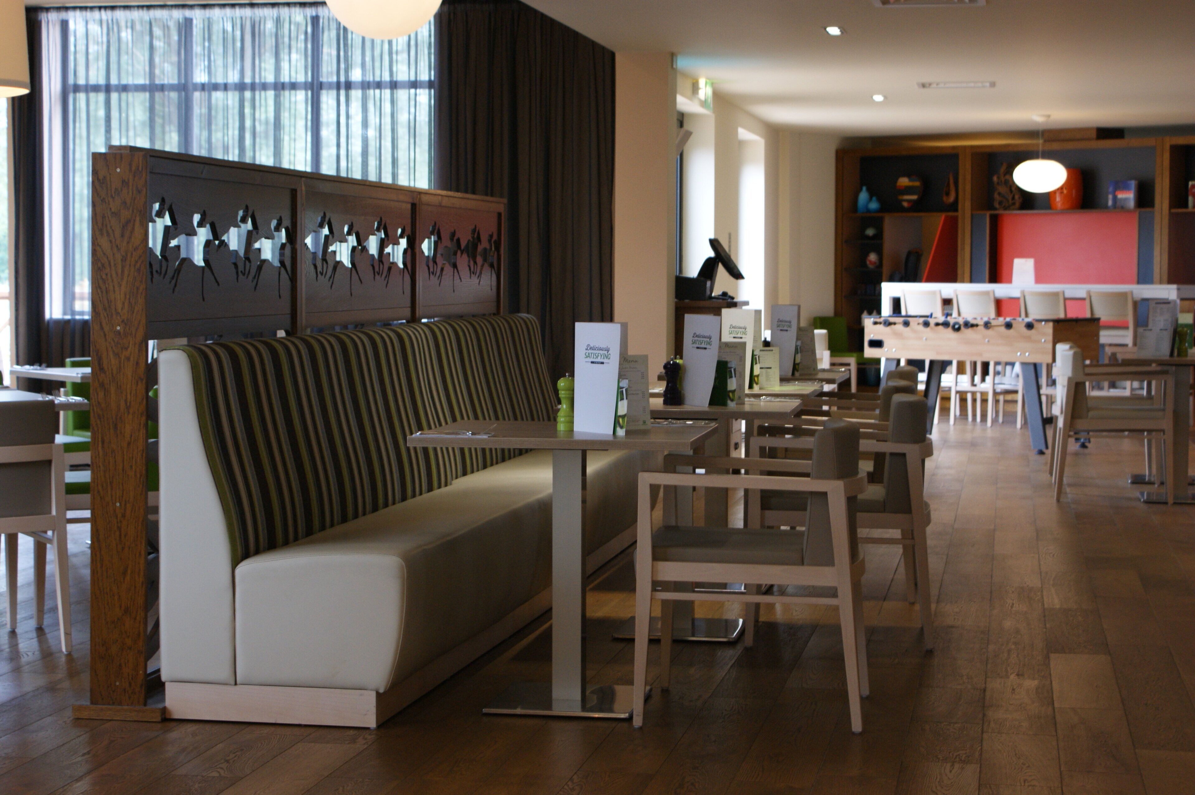 A modern restaurant interior with a long bench seating area, wooden tables, and chairs.