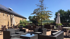 An outdoor patio with wicker furniture, umbrellas, and a view of the countryside. - Holiday Inn Huntingdon - Racecourse by IHG (Huntingdon)