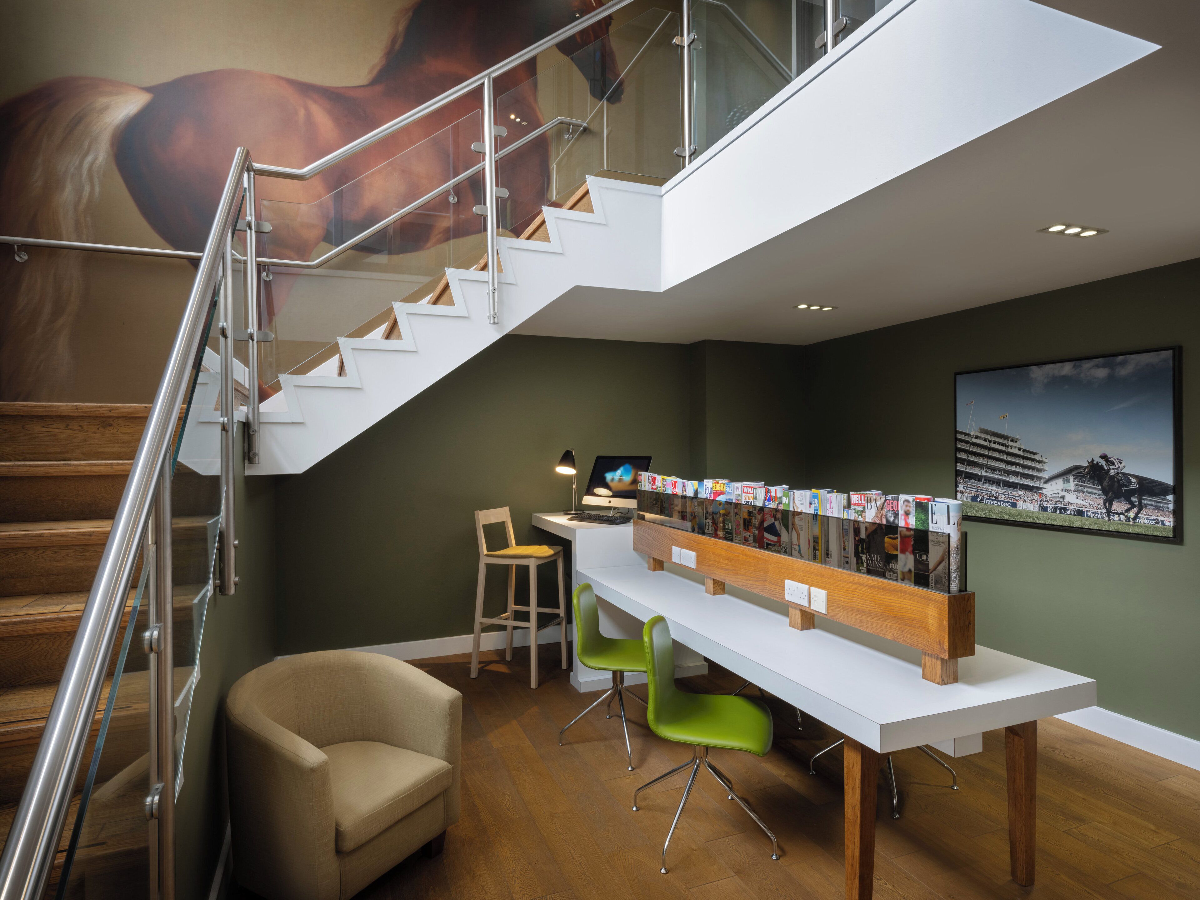 Un interior moderno con una escalera, un escritorio con revistas, una silla y un cuadro grande de un caballo en la pared.