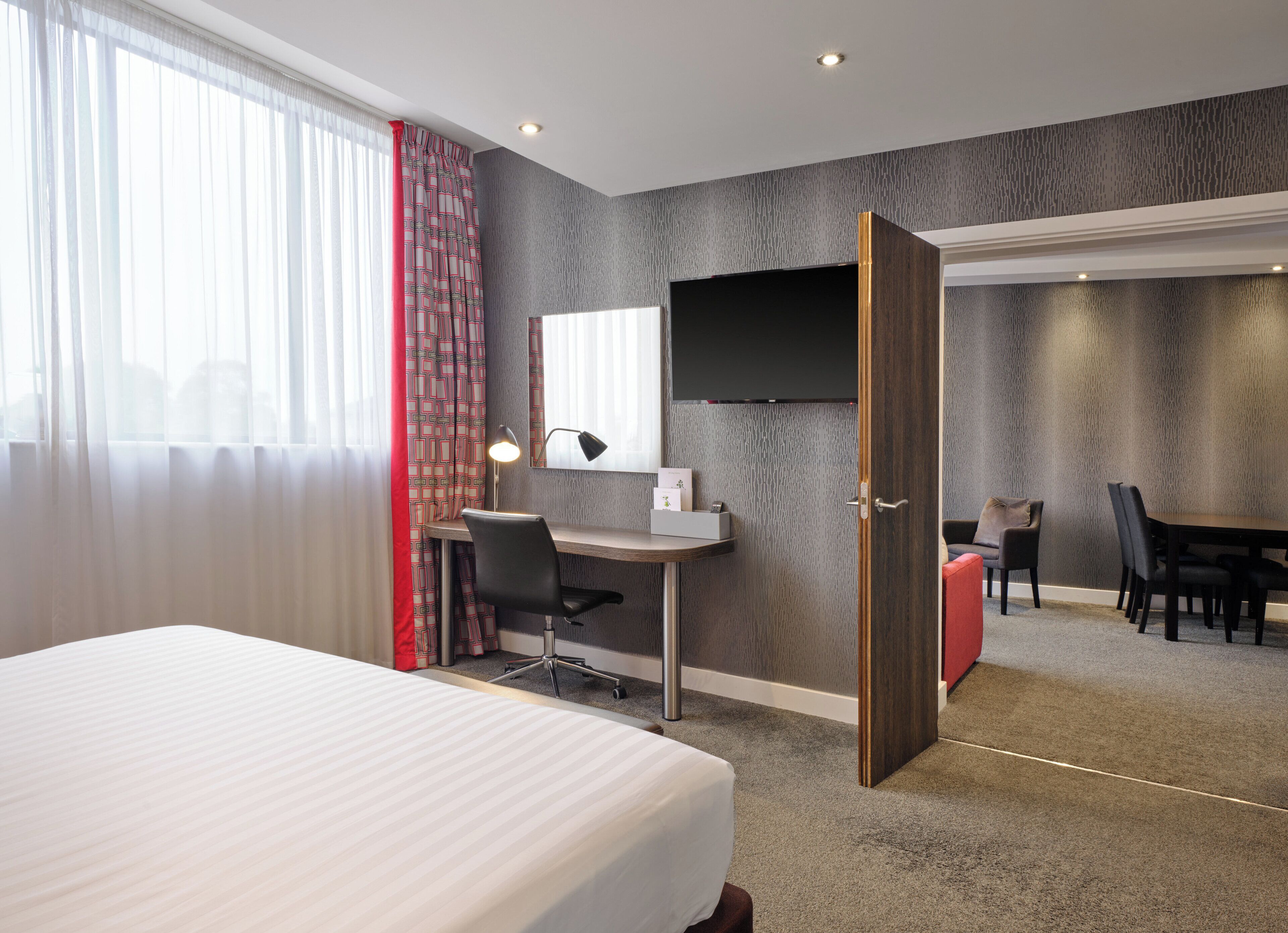 A hotel room with a bed, desk, chair, and a TV mounted on the wall.