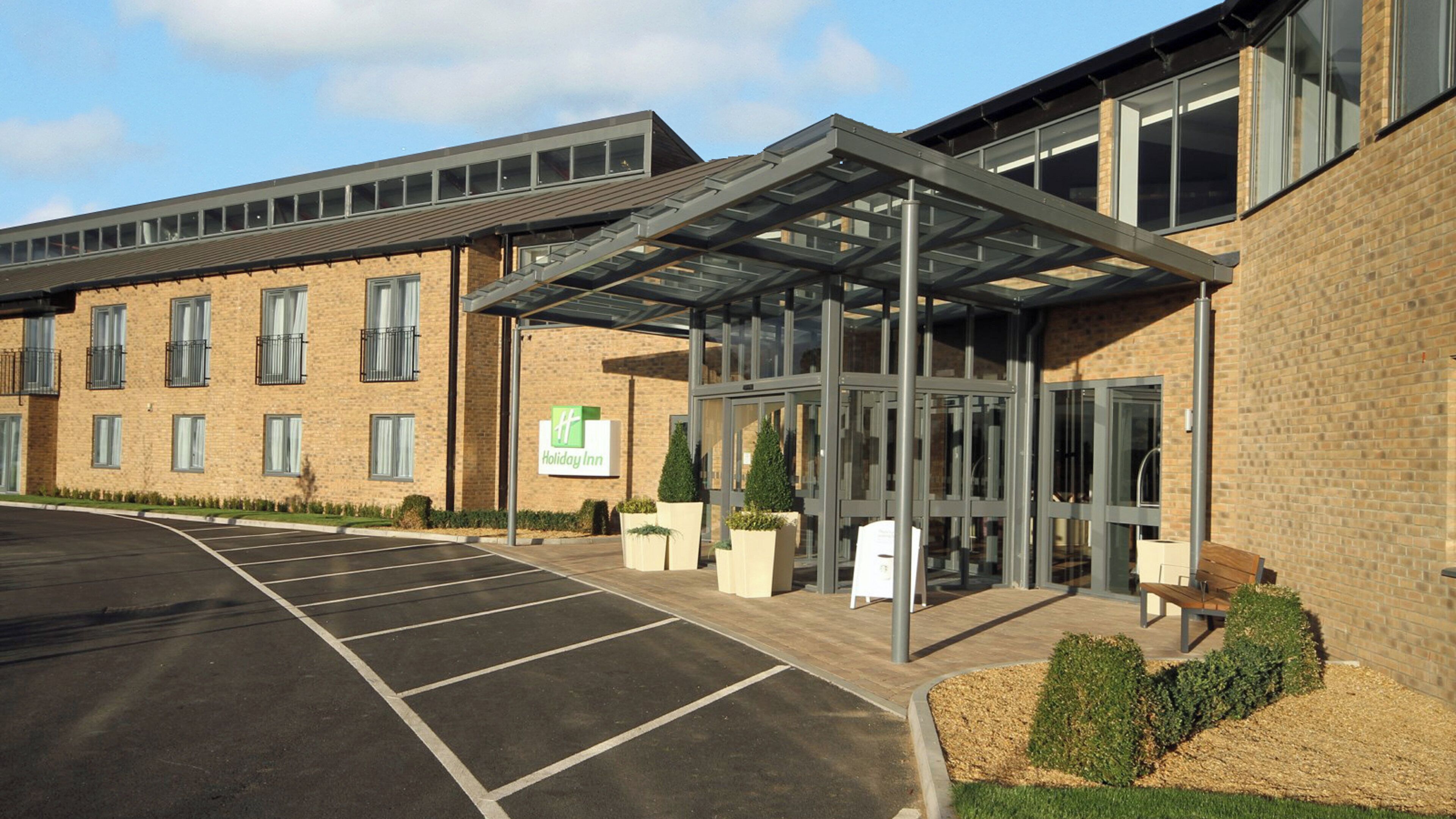 L’entrée d’un hôtel Holiday Inn, avec une allée couverte, un parking et une façade en briques.