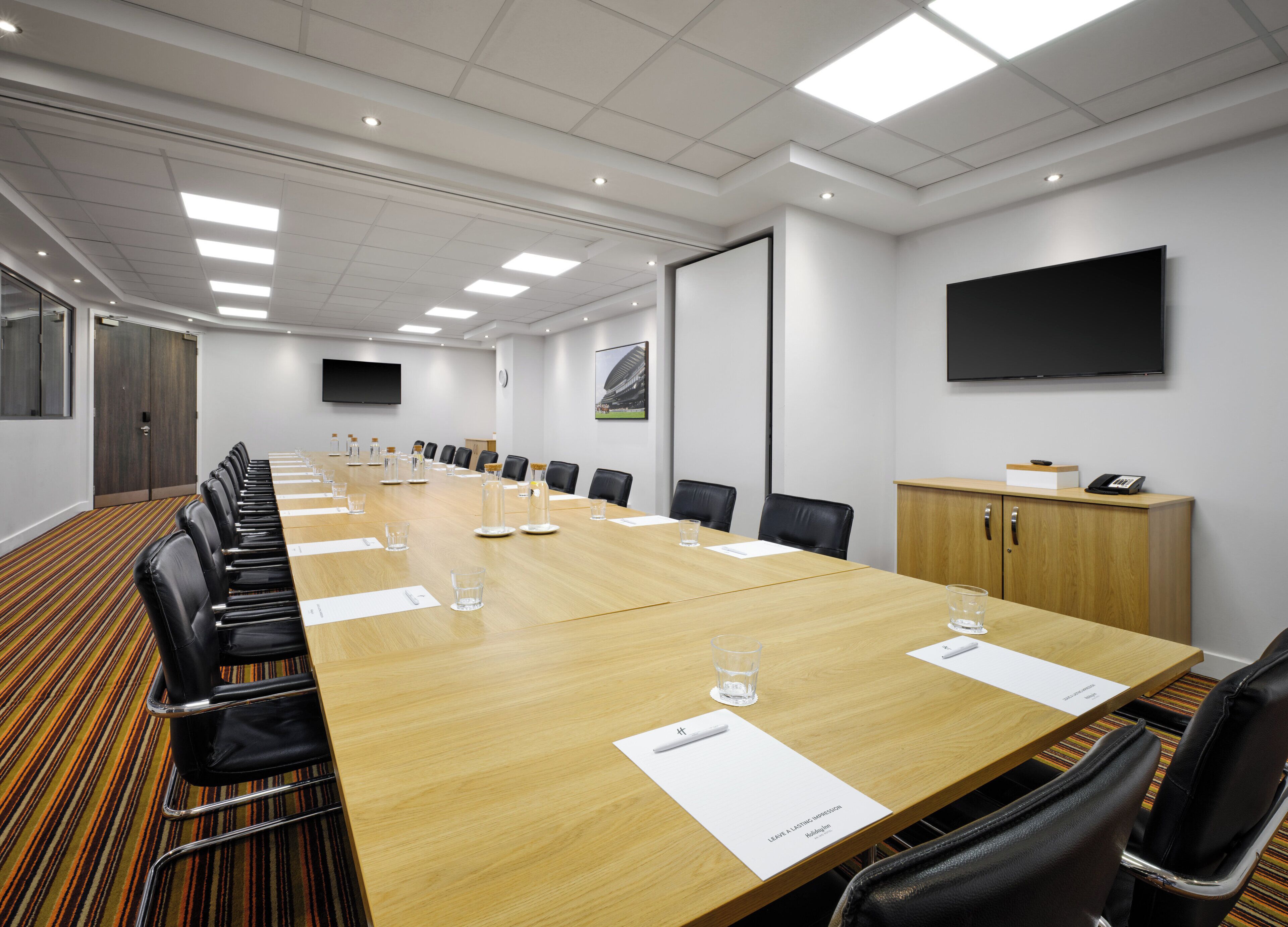 A conference room with a long table, chairs, a projector screen, and a wooden cabinet.
